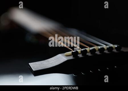 Schwarzer akustischer Gitarrensadel und Fixierstifte im Fokus. Professionelles Musikinstrument mit Metallsaiten Stockfoto