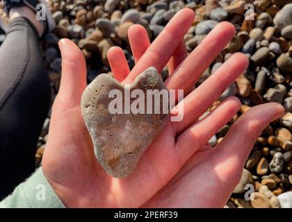 Herzförmiger Kiesel in den Händen - Brighton Beach - Brighton & Hove, East Sussex, Großbritannien Stockfoto
