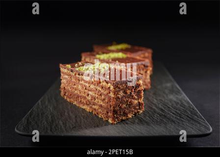 Schokoladenkuchen mit Walnüssen und Pistazien isoliert auf schwarzem Hintergrund. Gebäck aus hausgemachter Bäckerei Stockfoto