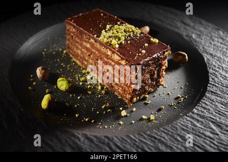 Schokoladenkuchen mit Walnüssen und Pistazien isoliert auf schwarzem Hintergrund. Gebäck aus hausgemachter Bäckerei Stockfoto