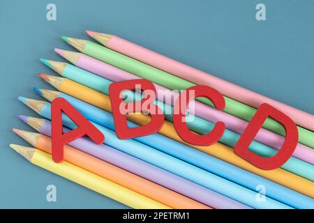 Back-to-School-Konzept mit verschiedenen Buchstaben und Buntstiften in Pastellfarben auf blauem Hintergrund Stockfoto