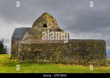 Ein traditionelles Steingebäude auf einer üppigen grünen Wiese mit einem düsteren Himmel im Hintergrund Stockfoto