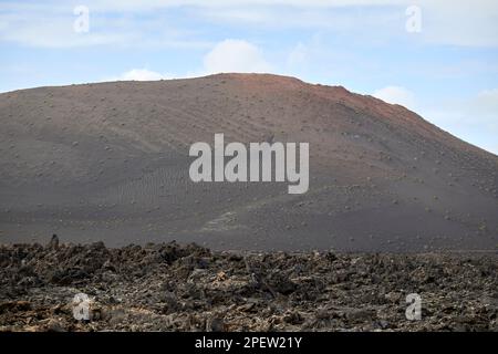 Blick über vulkanische Bomben, vulkanische Felsformationen und Lavafelder zu fernen Vulkanen bedeckt mit Pikon- und ascheparque nacional de timanfaya Lanzaro Stockfoto