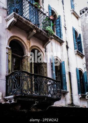 Ein kunstvoll verzierter Balkon aus Eisen und blaue Fensterläden in der Hinterstraße von Venedig, Italien. Stockfoto