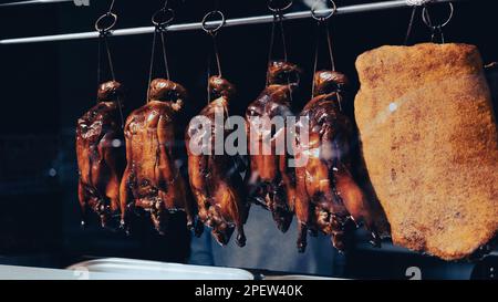 Gebratene knusprige Enten hängen an Metallhaken im Fenster eines chinesischen Restaurants Stockfoto