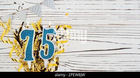 Blaue Festkerze Nummer 75 auf weißem Holzhintergrund mit goldener Folie. Speicherplatz kopieren. Stockfoto