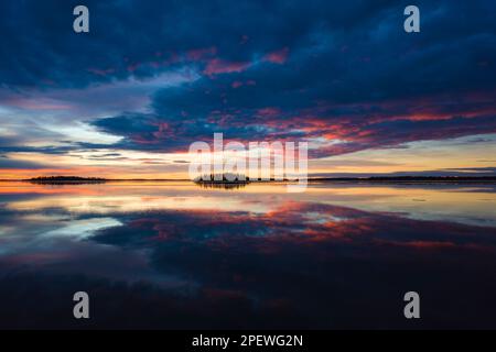 Herrlicher Sonnenaufgang über dem See Malaren in Schweden, ruhiges Wasser reflektiert den Himmel mit dramatischen Wolken, die von der Sonne rosa erleuchtet werden, orangefarbener gelber Horizont mit da Stockfoto