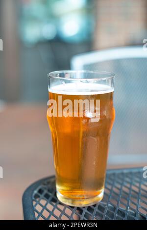 Ein Glas indisches, helles Craft-Bier mit weißem Schaum auf dem Kopf. Die goldene Flüssigkeit besteht aus einem orangefarbenen Bier in einem hohen, klaren Pint-Glas. Stockfoto