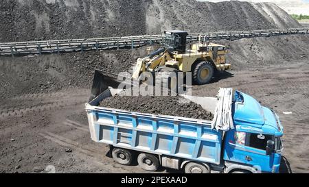 Radlader, der Kohle auf Lkw lädt und auf einer riesigen Bergbaustelle arbeitet. Stockfoto