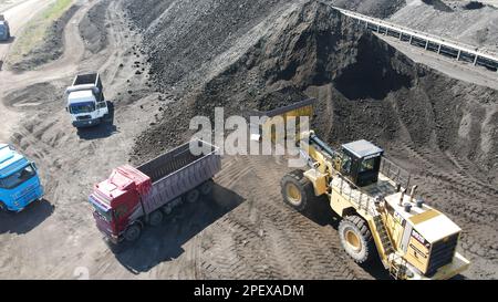 Radlader, der Kohle auf Lkw lädt und auf einer riesigen Bergbaustelle arbeitet. Stockfoto