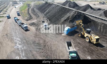 Radlader, der Kohle auf Lkw lädt und auf einer riesigen Bergbaustelle arbeitet. Stockfoto