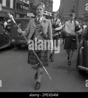 1955, historisch, Rag Week, ein stolzer schottischer Student in seinem Kilt und mit einem Pfeffer, der als Trommelprofessor agierte und eine Scottsh-Pfeifenband durch die Straße in Cambridge, England, Großbritannien, führte, Die RAG Week war eine Handelszeit an Universitäten und Hochschulen, in der verschiedene Veranstaltungen von Studenten organisiert werden, um Geld für wohltätige Zwecke zu sammeln. Eine Prozession durch die lokale Stadt - wie hier zu sehen - mit dekorierten Wagen war oft das Hauptereignis der „Rag“-Feier. Der Begriff soll von dem Verb „zu Rumpeln“ abgeleitet sein, das heißt, zu belästigen, wo die Studenten Leute „zerfleischt“ haben, um sie für wohltätige Zwecke zu spenden. Stockfoto