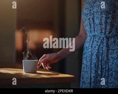 Die Frau trinkt Kaffee, Morgenroutine. Kleines Haus. Erstes Grundstück. Kleine Inneneinrichtung des Apartments. Minimalismus. Wir ziehen ein. Allein zu leben. Charmantes Wohnwagenhaus mit Morgensonne Stockfoto