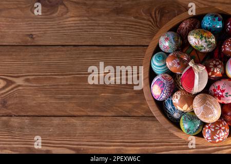 Eine Holzschüssel mit eng angeordneten Ostereiern steht auf einem Hintergrund mit Brettern. Stockfoto