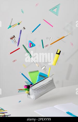 Eine silberne Federmäppchen mit bunten Schulartikeln, die über dem Tisch schwebt. Stockfoto