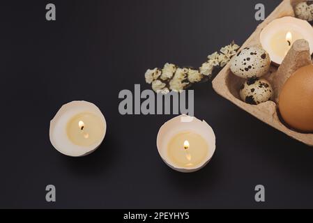Osterkarte mit Kerzen in Eierschale und Tablett mit Ei auf dunklem Hintergrund. Weiße Blume. Urlaub wird mit Ihren eigenen Händen gemacht. Kreativer Ansatz. Bereich Kopieren Stockfoto