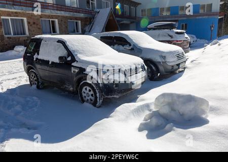 Schneebedeckte Autos auf dem Parkplatz vor dem ukrainischen Hotel, Geländewagen im Schnee in den Bergen Stockfoto