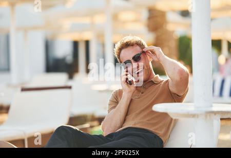 Sitzt und benutzt das Telefon. Der junge Mann ist tagsüber draußen. Urlaubskonzept Stockfoto