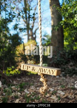 Nahaufnahme einer Seilschaukel in freier Wildbahn mit den Worten „Up & Away“ auf dem Holz, die Konzepte von Freiheit, Wohlbefinden und Verbundenheit mit der Natur zum Ausdruck bringen Stockfoto