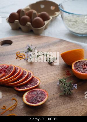 Nahaufnahme der Backzutaten auf einem Tisch, einschließlich Blutorangen, Rosmarin, Mehl und Eier zur Zubereitung eines hausgemachten Kuchen Stockfoto