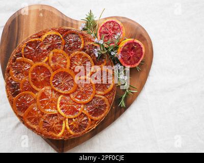 Blut-Orange-Upside-down-Kuchen und Rosmarin-Zierleiste, von oben auf einem herzförmigen Servierbrett auf weißem Hintergrund mit Platz für Kopien aufgenommen Stockfoto