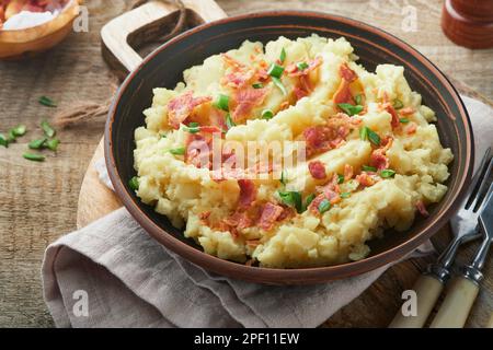 Kartoffelbrei. Kartoffelpüree mit Speck und grünen Zwiebeln, Pfeffer und Cheddar in der Schüssel auf altem Holzhintergrund. Leckeres cremiges Kartoffelpüree Stockfoto