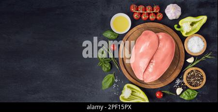 Rohe Hähnchenfilets auf Holzbrettern und Gewürzen, Kräuter zum Essen auf einem Tisch aus schwarzem Stein. Draufsicht Stockfoto
