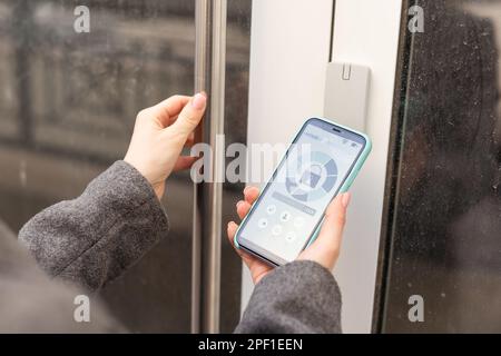 Frau, die smartlock an der Eingangstür mit einem Smartphone verriegelt. Konzept der Verwendung intelligenter elektronischer Schlösser mit schlüssellosem Zugang. Stockfoto