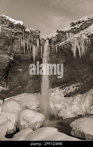 Gruppe von Bergsteigertouristen hinter dem gefrorenen Kvernufoss Wasserfall, mit Schnee und Stalagamiten, wobei das Wasser in die gefrorenen Flüsse von mir fällt Stockfoto