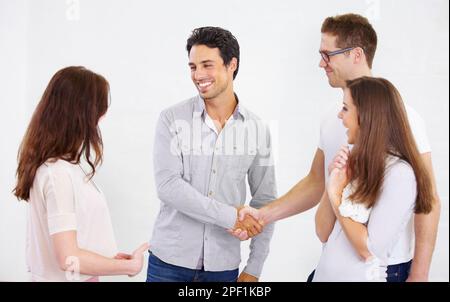 Er ist auf der Erfolgsleiter. Zwei junge Geschäftsleute schütteln sich die Hand, während ihre Kollegen zuschauen. Stockfoto