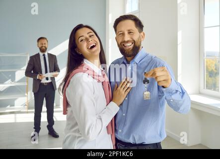 Glückliches Paar, das neue Hausschlüssel vor der Kamera zeigt Stockfoto