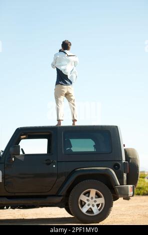Ich muss höher. Ein junger Mann, der für eine bessere Aussicht ins Auto steigt. Stockfoto