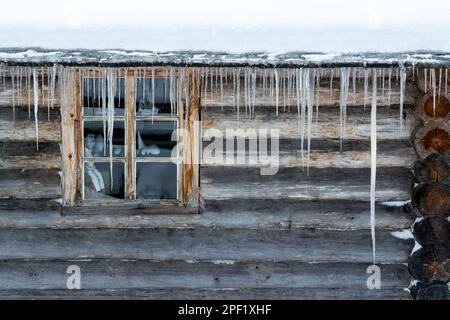 Rechteckiges Fenster an einer Holzwand und große Eiszapfen, die von den Dachrinnen hängen. Aus der Serie Window of the World. Stockfoto