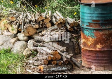 OD rostiges Eisenfass zum Verbrennen von Müll auf einem Landgarten und Brennholz auf Steinen. Stockfoto