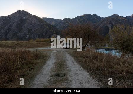 Eine alte Automarke „Honda HR-V“ steht in der Ferne der Straße unter den Bergen und Felsen in der Nähe des Flusses im Altai in Sibirien. Altai, Russland - Stockfoto