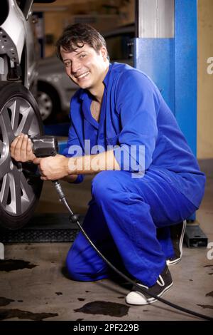 Die neuen Reifen aufziehen. Porträt eines männlichen Mechanikers, der am Rad eines Autos arbeitet. Stockfoto