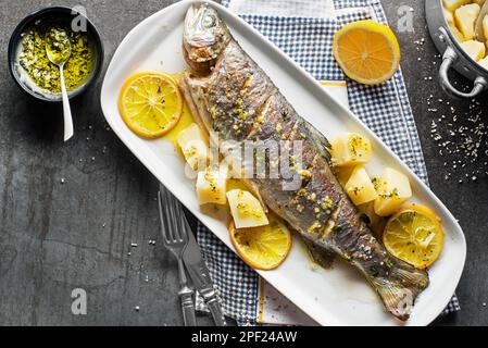 Gebratene traditionelle Flusforelle mit Salat, Kartoffeln und (Knoblauch, Petersilie) Sauce auf grauem Tischhintergrund Stockfoto