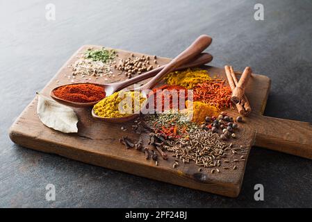 Bunte Kräuter und Gewürze zum Kochen. Indische und asiatische Gewürze auf grauem Steinhintergrund. Stockfoto