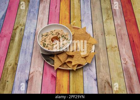 Schüssel aus weißem Porzellan mit Thunfisch in Chipotle Sauce mit Mais-Tortilla-Chips auf einem farbigen Tisch Stockfoto