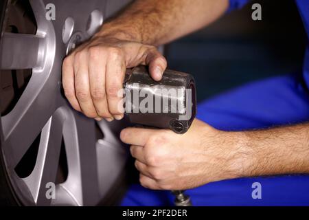 Er hat viel Erfahrung mit der Reifenmontage. Zugeschnittenes Bild eines Mechanikers, der am Lenkrad eines Autos arbeitet. Stockfoto