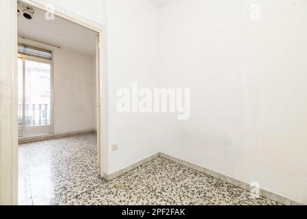 Kleines, leeres Zimmer eines Hauses mit Terrazzo-Böden mit schwarzen Punkten und Ausgang zu einem Zimmer mit Balkonen zur Straße mit Aluminium und Glas Schieber Stockfoto