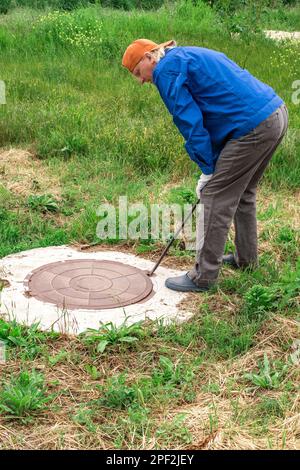 Der Versorgungsanwärter überprüft den Wasserzähler im Brunnen, indem er den Brunnenschacht öffnet. Stockfoto