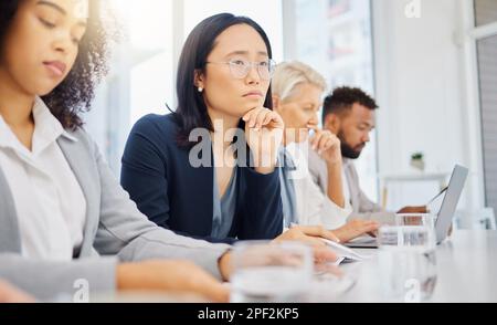 Eine seriöse junge asiatische Geschäftsfrau, die eine Brille trägt und mit der Hand am Kinn denkt, während sie einem Präsentationsmeeting in einem Konferenzraum zuhört Stockfoto
