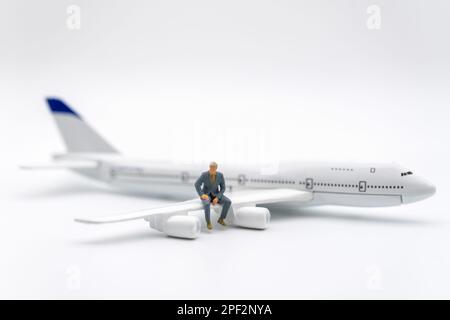 Business- und Reisekonzept. Geschäftsmann Miniaturfigur Leute sitzen auf einem Flügel eines Flugzeugspielzeugmodells auf weißem Hintergrund. Stockfoto