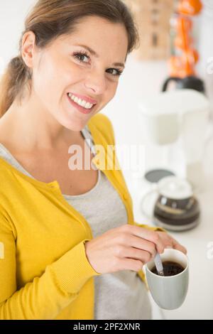 Glückliche Frau, die Zucker mit einem Löffel in den Kaffee schüttet Stockfoto