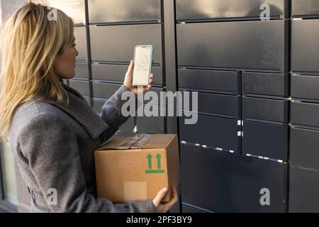 Schöne Frau, die ein Paket aus einem intelligenten elektronischen Paketschließfach aus Stahl abholt, automatische Briefkästen. Paczkomat-Lieferservice, Abholung Stockfoto