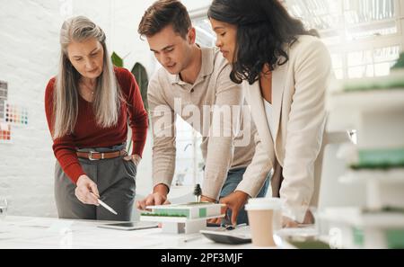 Eine reife Geschäftsfrau, die mit dem Personal über einen Plan spricht. Der leitende Chef arbeitet mit den Mitarbeitern zusammen, um den Bauplan mit einem Tablet zu erstellen. Geschäftsleute, die Drogen nehmen Stockfoto