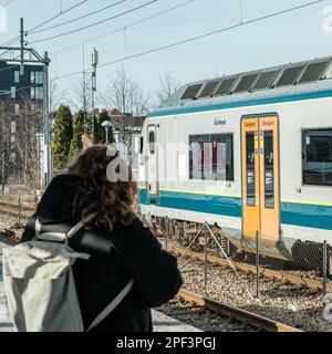 Sandnes, Norwegen, 10 2023. März, Frau mit Rucksack, die auf den Zug wartet, mit NSB Klasse 72 Locomotive in Backgorund am Bahnhof Sandnes Stockfoto