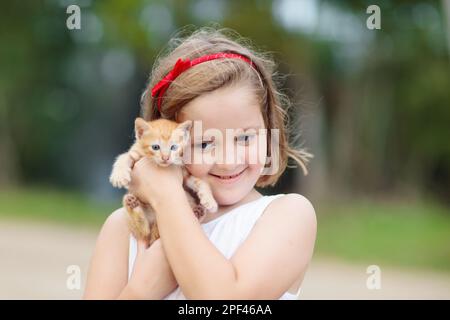 Kind, das eine Katze hält. Kinder und Haustiere. Kleines Mädchen umarmt niedlichen kleinen Kätzchen im Sommergarten. Haustiere in der Familie mit Kindern. Stockfoto