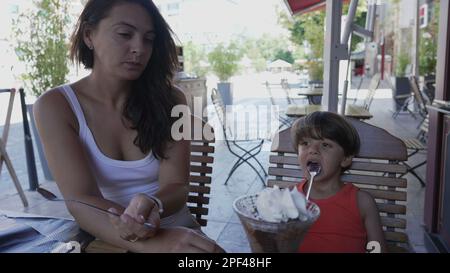 Mutter und Kind teilen sich nach dem Mittagessen ein Eis zum Abendessen im Restaurant. Süßes Dessert mit geschlagener Kirschcreme Stockfoto